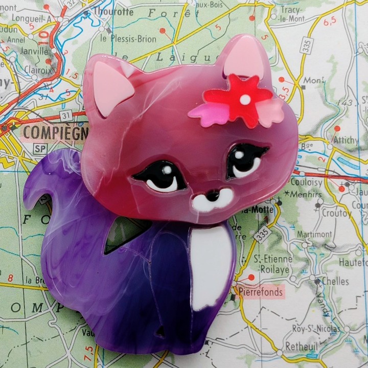 broche fantaisie chaton malicieux, avec son pelage violet lumineux et sa pince fleurie.