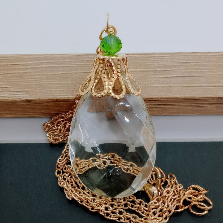 Gros plan sur la perle vert émeraude sacrée fantaisie et la coiffe dorée travaillée style rétro du collier talisman.