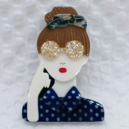 Broche en acrylique femme, chignon brun, serre-tête bleuté, lunettes jaunes pailletées, chemise bleue à pois