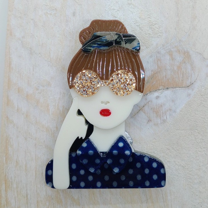 Broche en acrylique femme, chignon brun, serre-tête bleuté, lunettes jaunes pailletées, chemise bleue à pois