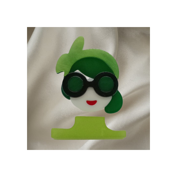 broche femme stylée avec ses cheveux verts, lunettes noires et tenue vert clair.